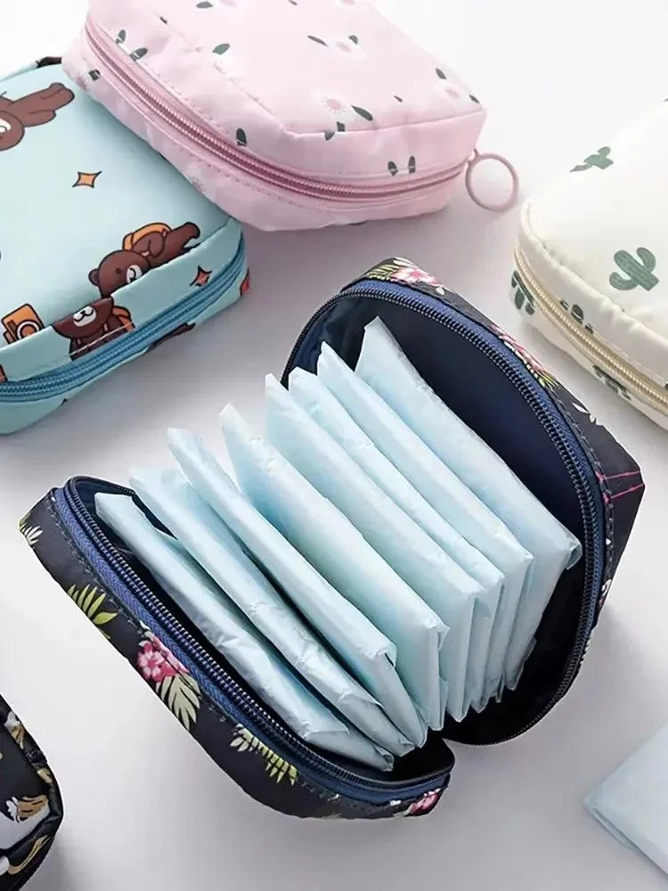 A collection of light blue sanitary napkins is neatly stored in a black zippered pouch alongside pink and teal storage pouche
