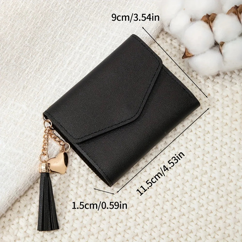 Black PU leather coin clutch wallet with a gold chain and tassel resting on a cream textured fabric.