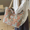 A person holds a patterned bohemian corduroy tote bag with light floral designs.
