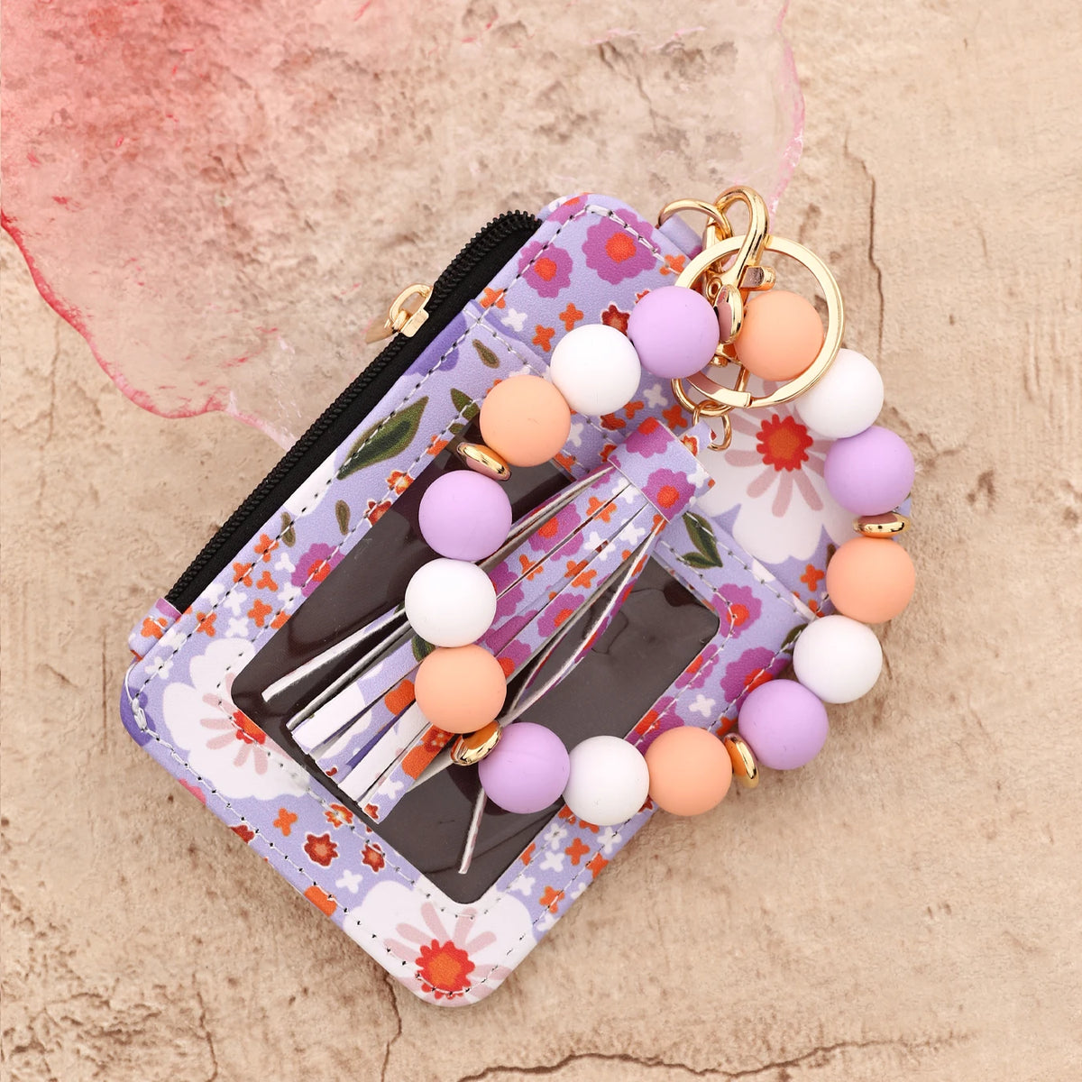 Cartera llavero de cuero PU silicona floral rosa con pulsera de cuentas sobre una superficie beige clara.