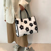 A woman holds a white and black leopard print faux fur designer shoulder tote bag while wearing a beige coat and trousers.