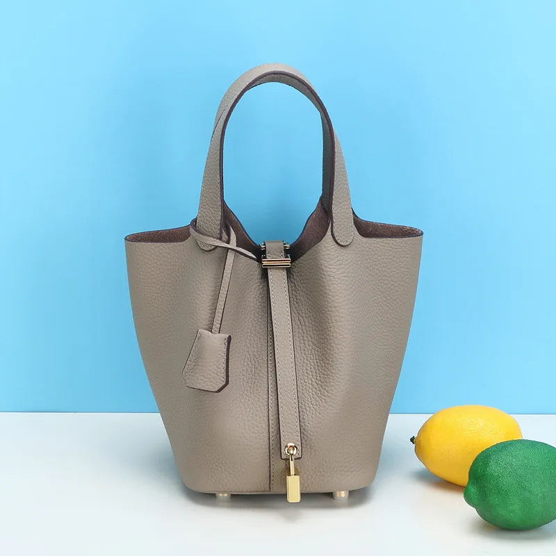 Beige Leder-Bucket-Bag mit Henkel und goldfarbenem Hardware auf weißem Untergrund