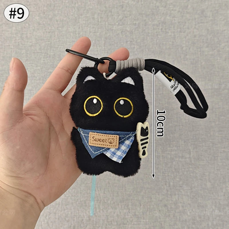 Colgante de gato negro de peluche en forma de llavero, con ojos bordados y una etiqueta de tela a cuadros azules.