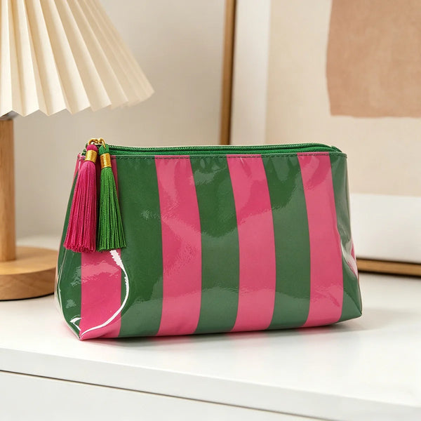 Bolsa de viaje cosmética a rayas verdes y rosas con flecos dorados sobre una superficie blanca.