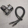 A black digital camera with a strap is shown against a gray fabric background.