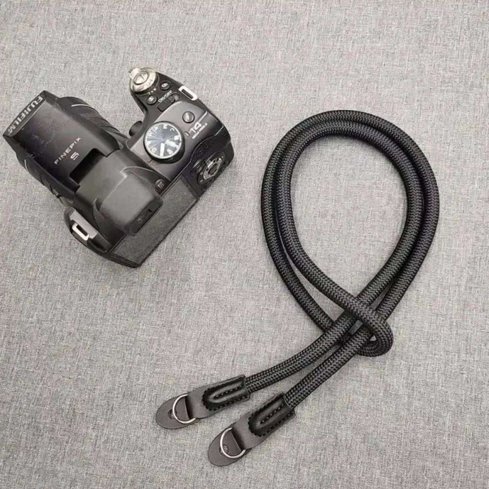 A black digital camera with a strap is shown against a gray fabric background.