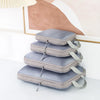A stack of four gray travel compression packing cubes with fabric straps on a white surface.