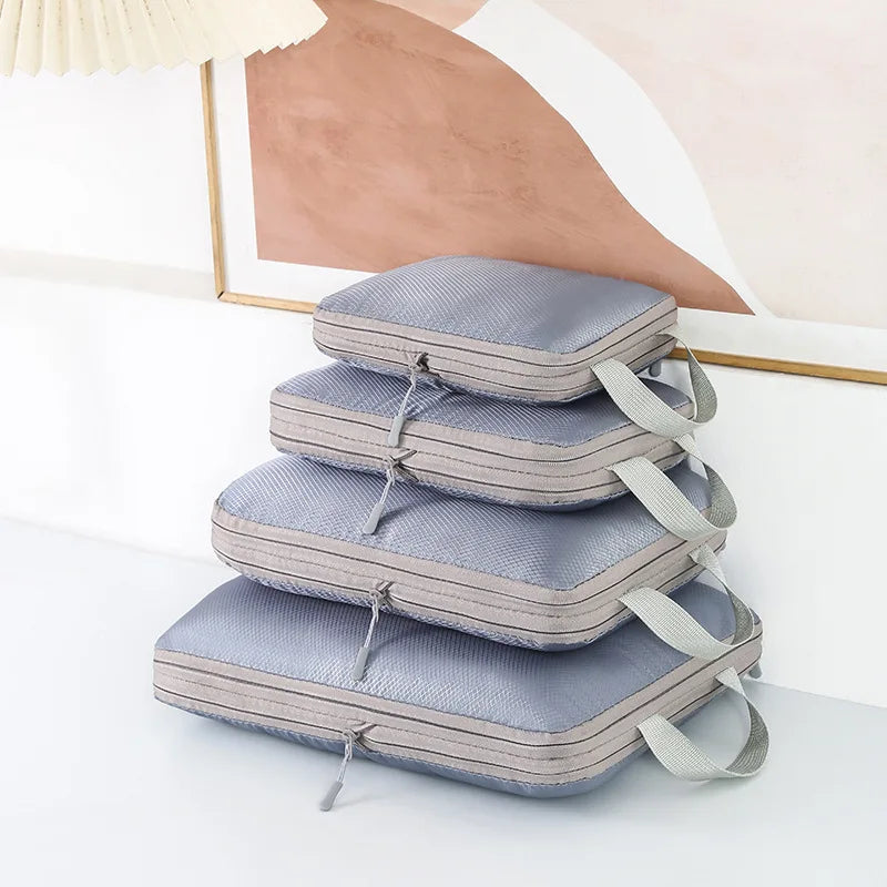A stack of four gray travel compression packing cubes with fabric straps on a white surface.