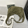 Olive green cotton canvas shoulder crossbody bag resting on a gray surface next to a digital clock and a book.