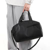 A black waterproof travel duffle bag with a separate shoe compartment being held by a person.