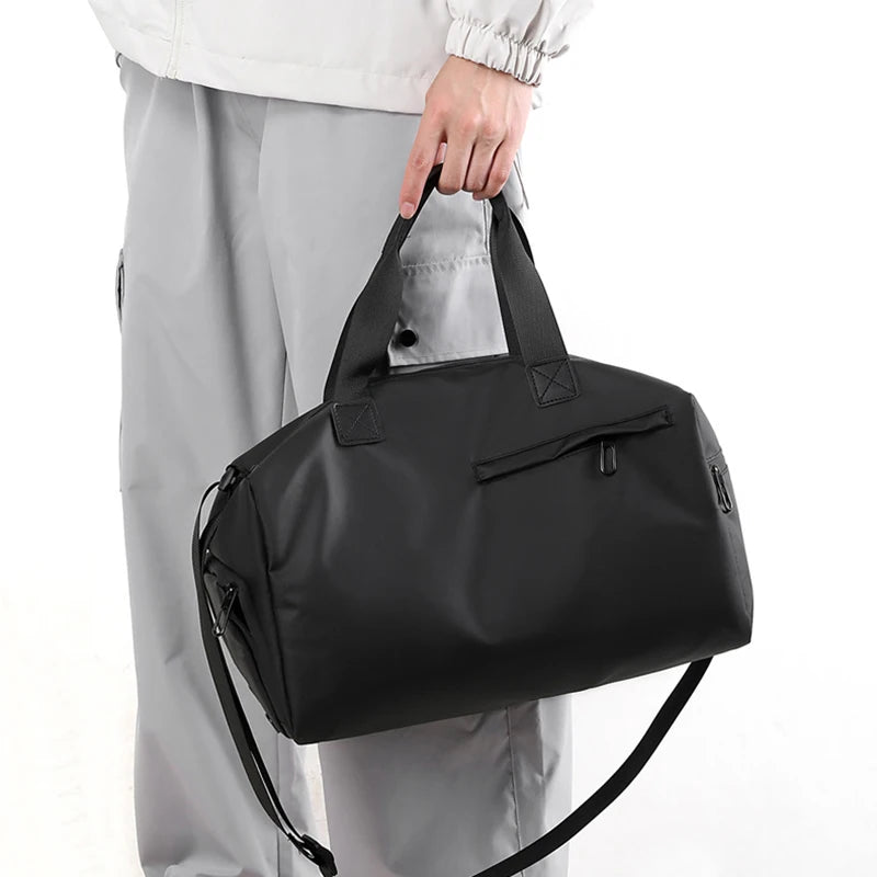 A black waterproof travel duffle bag with a separate shoe compartment being held by a person.