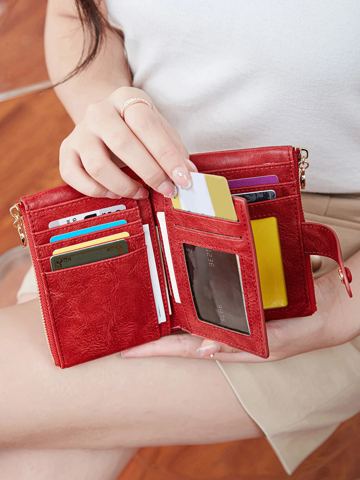 A hand holds an open red leather card holder wallet displaying various cards and cash.
