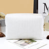 A white ribbed makeup organizer bag with a zippered closure is displayed on a white surface.