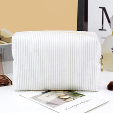 A white ribbed makeup organizer bag with a zippered closure is displayed on a white surface.