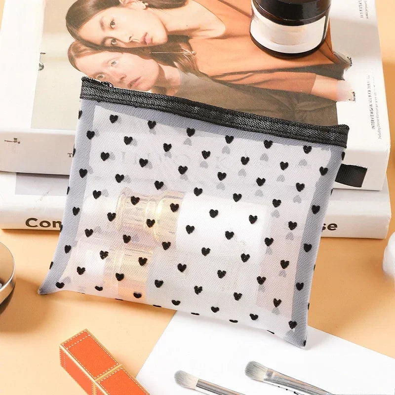 A clear mesh cosmetic storage pouch with black trim and small black hearts is shown next to skincare products.