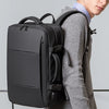 A man wearing a grey sweater holds a black men's business travel backpack.