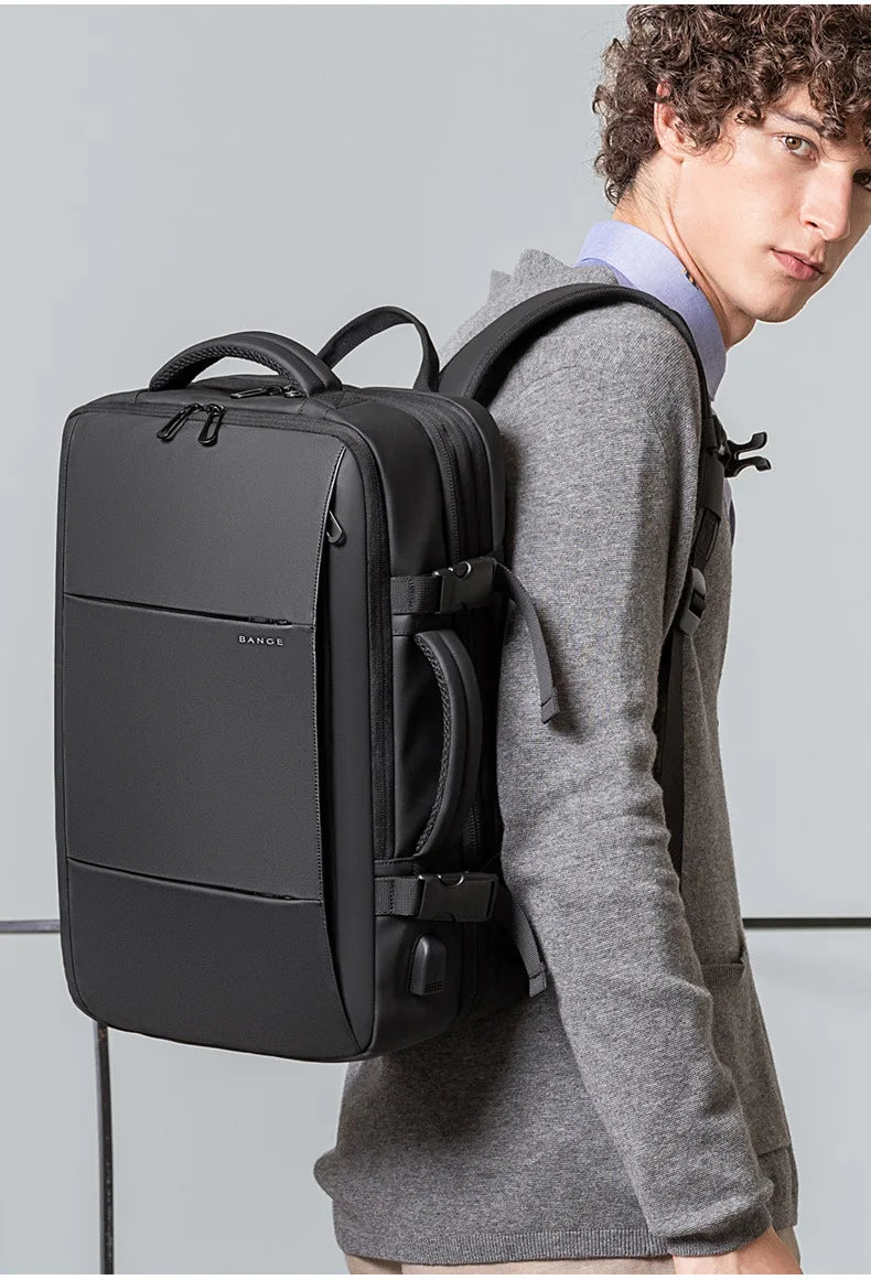 A man wearing a grey sweater holds a black men's business travel backpack.