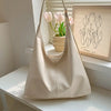 A beige PU leather slouchy hobo shoulder bag with a strap, placed on a white shelf next to a framed art print.
