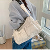 A person is holding a beige and white striped nylon drawstring tote bag over their shoulder.