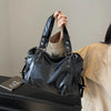 A black leather shoulder bag is held by a person against a light gray background.