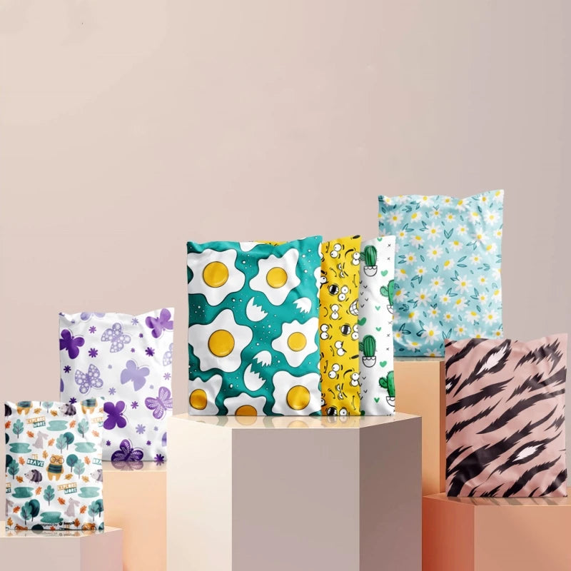 Collection de sacs d'envoi à motif floral colorés empilés sur une surface rose pâle.
