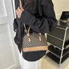 A woman holds a tan and black patterned fashion shell shoulder crossbody bag against a white background.