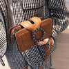 A close-up of a vintage brown PU leather crossbody bag with a rhinestone buckle held by a person wearing a black and white st