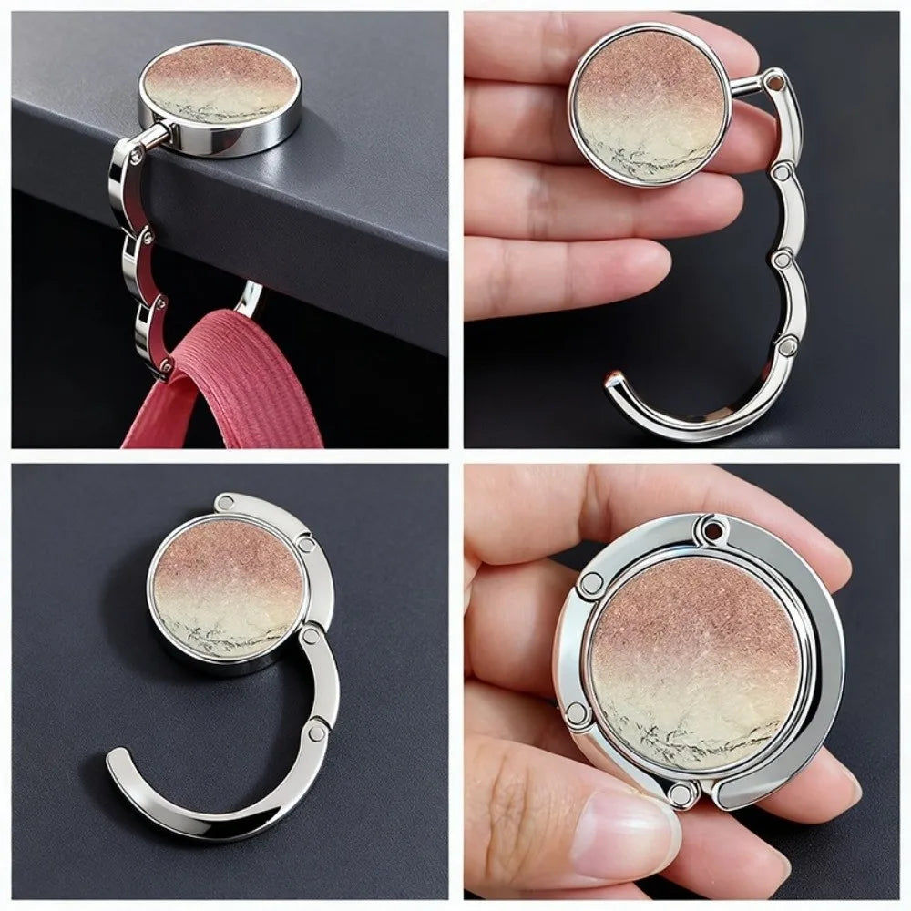 A round silver metal bag hanger with a curved hook is shown in various angles and on a hand.