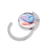 Silver folding table bag hook with a round clear dome featuring a colorful butterfly and marble sky design