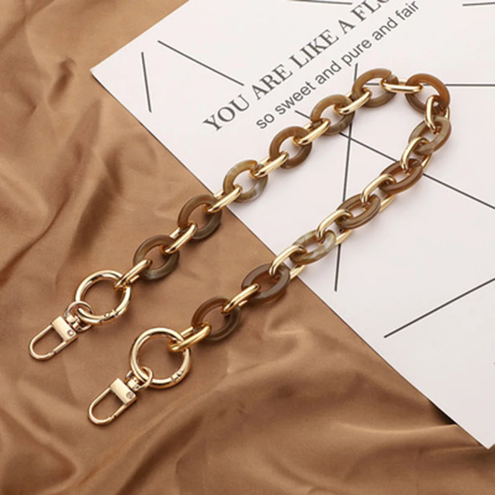 A gold-toned acrylic handbag strap chain laid across a piece of paper on brown fabric.