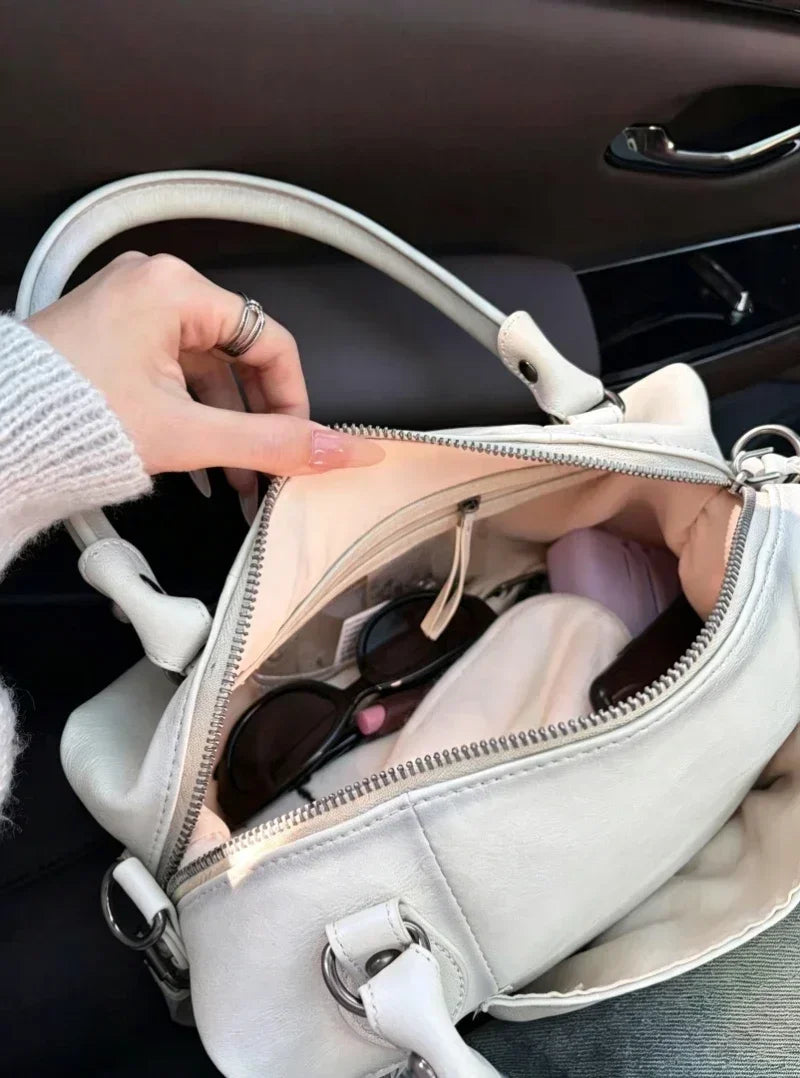A close-up of a white PU leather crossbody shoulder bag with silver hardware resting on a dark car seat.