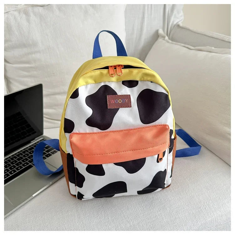 A women's cow print fashion backpack in white and black with yellow trim and blue straps.
