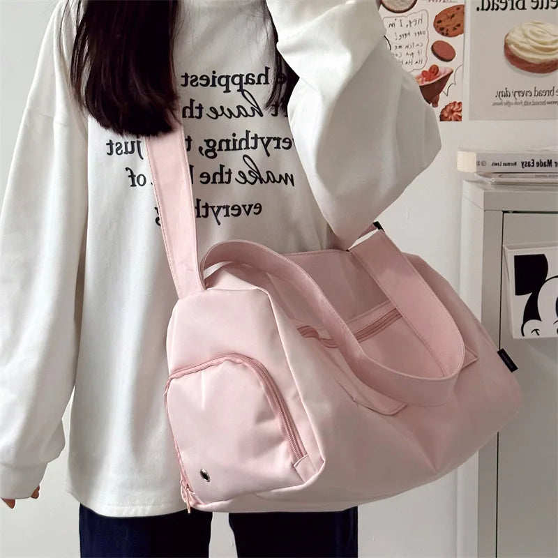 A pink canvas crossbody travel tote bag is shown being held by a person wearing a white long-sleeved shirt.
