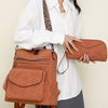 A woman is holding a retro brown PU leather travel backpack and a matching clutch against a light background.
