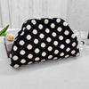 A black and white polka dot clutch bag is displayed on a white surface next to a light green flower.