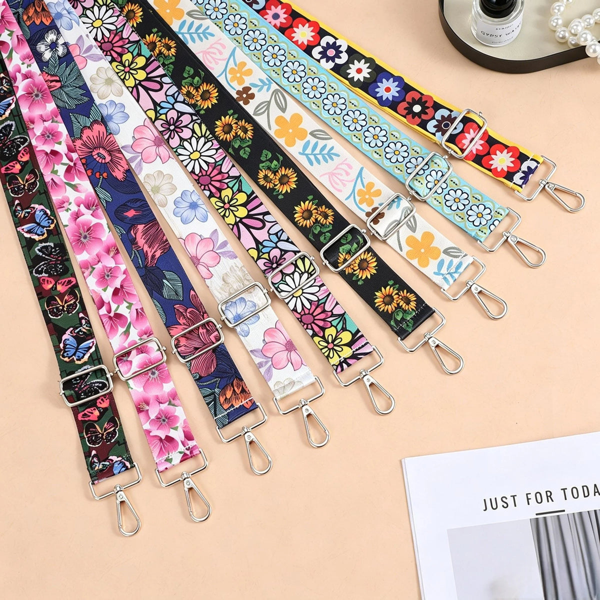A collection of colorful floral patterned nylon crossbody bag straps with metal buckles laid out on a light background.