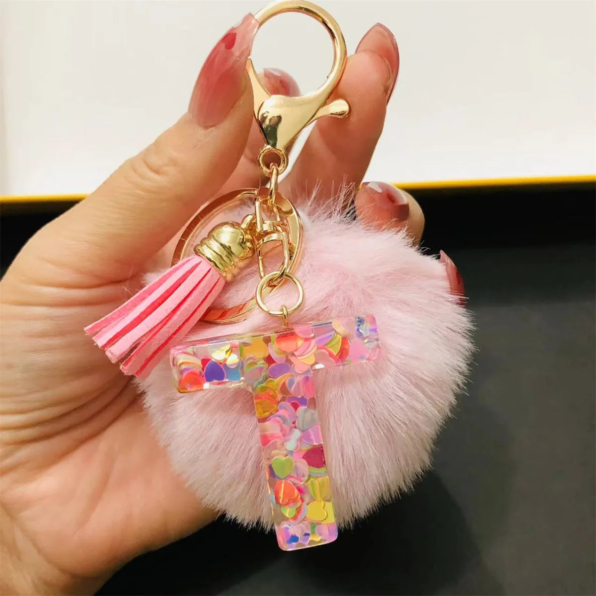 A hand holds a custom initial letter keychain featuring a shiny resin pendant and pink alphabet charm.
