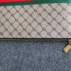 Beige Gucci Monogramm-Clutch mit grün-rotem Zierrand auf grauem Stoff