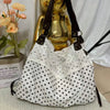 A white fabric shoulder bag with black polka dots and a floral pattern, displayed next to a gold decorative object.