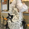 A woman holds a white corduroy bow print backpack with black ribbon details in a store setting.