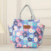 Bolsa térmica floral morada y rosa con asas grises mostrada sobre una superficie blanca.
