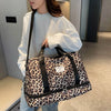 A woman holds a leopard print travel duffel bag with a shoe compartment in a light gray sweater.