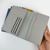 A hand holds an open customizable PU leather passport holder with multiple colored card slots.