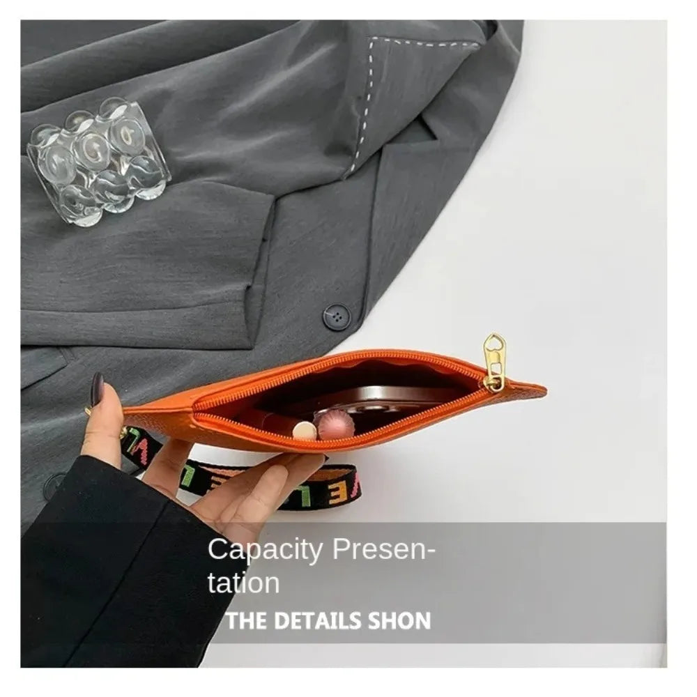 Cartera de monedas de corazón naranja de PU sostenida contra tela de blazer gris.