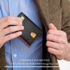 A hand holds a black carbon fiber minimalist trifold wallet against a blue striped shirt and brown jacket.