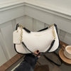 A white leather shoulder bag with gold chain details is held by a hand against a light background.