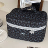 A dark floral patterned quilted cosmetic bag with a silver zipper and bow on a white surface.