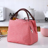 A red and white striped thermal lunch bag with brown handles resting on a white table.
