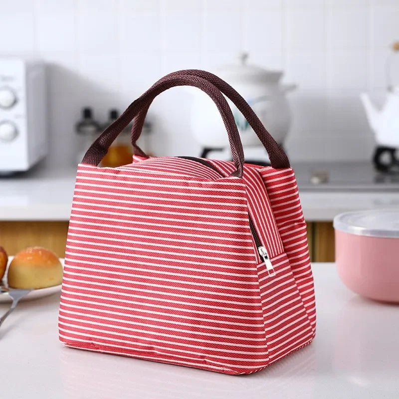 A red and white striped thermal lunch bag with brown handles resting on a white table.