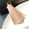 A set of light pink leather tassel fringe craft supplies displayed on a white plate.